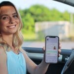 Smiling Woman In Car Holding Up A Smartphone.
